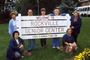 Senior_citizens_gathered_around_sign-300x199